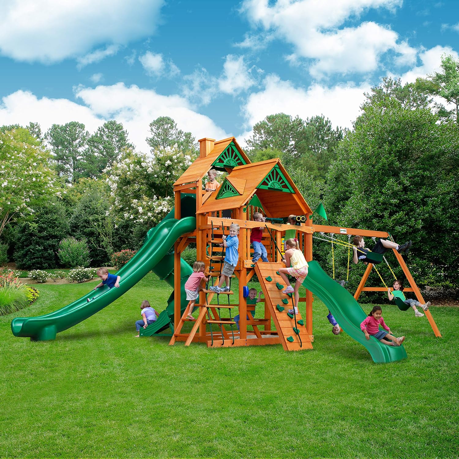Brown wooden swing set with attached roof, three slides, and climbing rock wall for preschool-age children — view 1