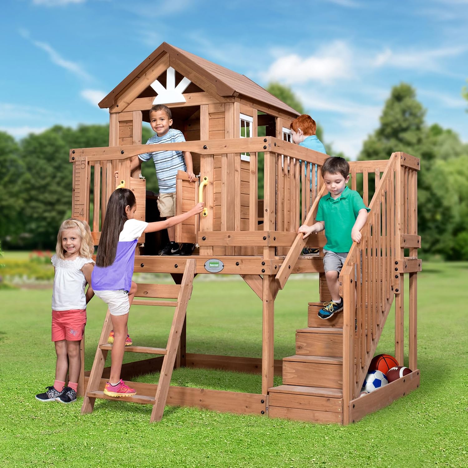 Elevated cedar wooden playhouse with integrated play kitchen, wrap-around deck, and saloon-style doors for outdoor play — view 1