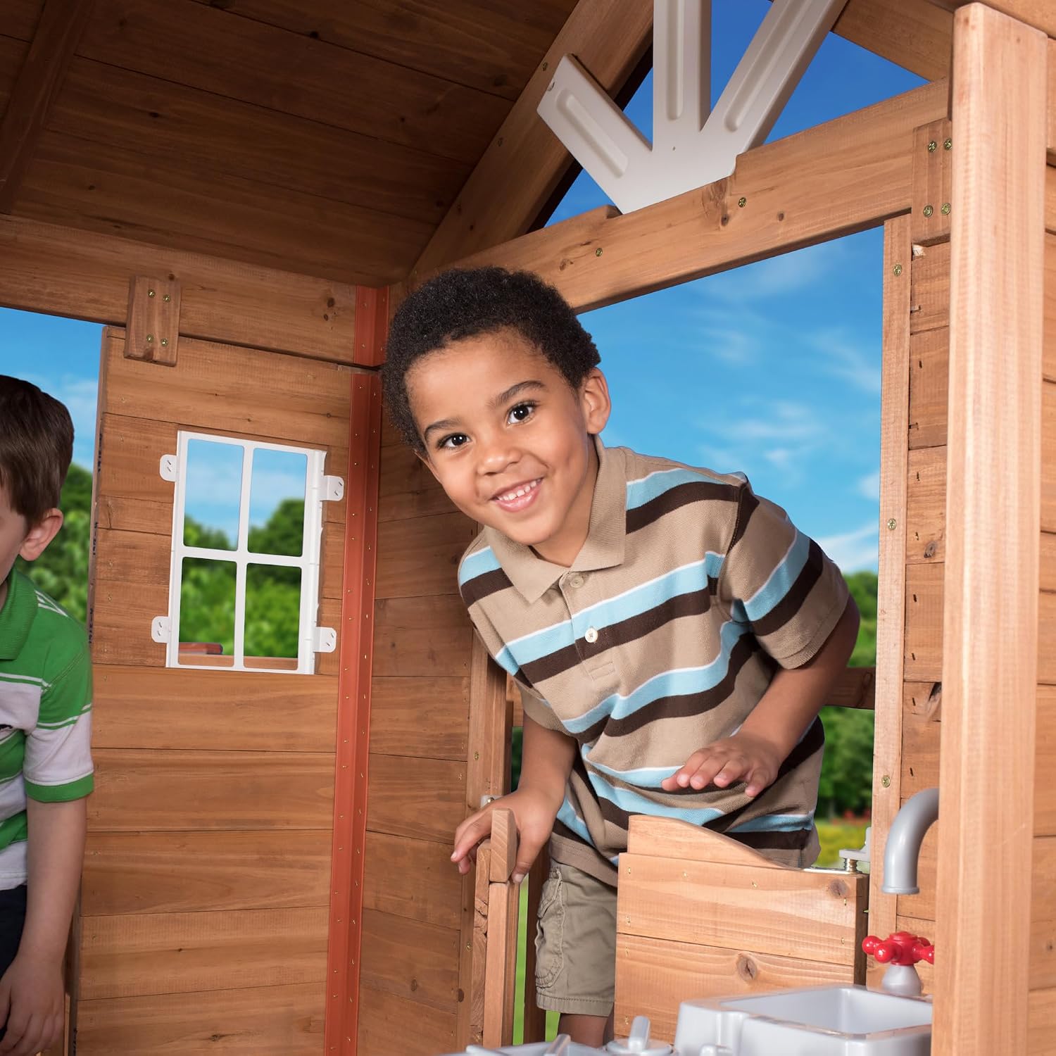 Elevated cedar wooden playhouse with integrated play kitchen, wrap-around deck, and saloon-style doors for outdoor play — view 2
