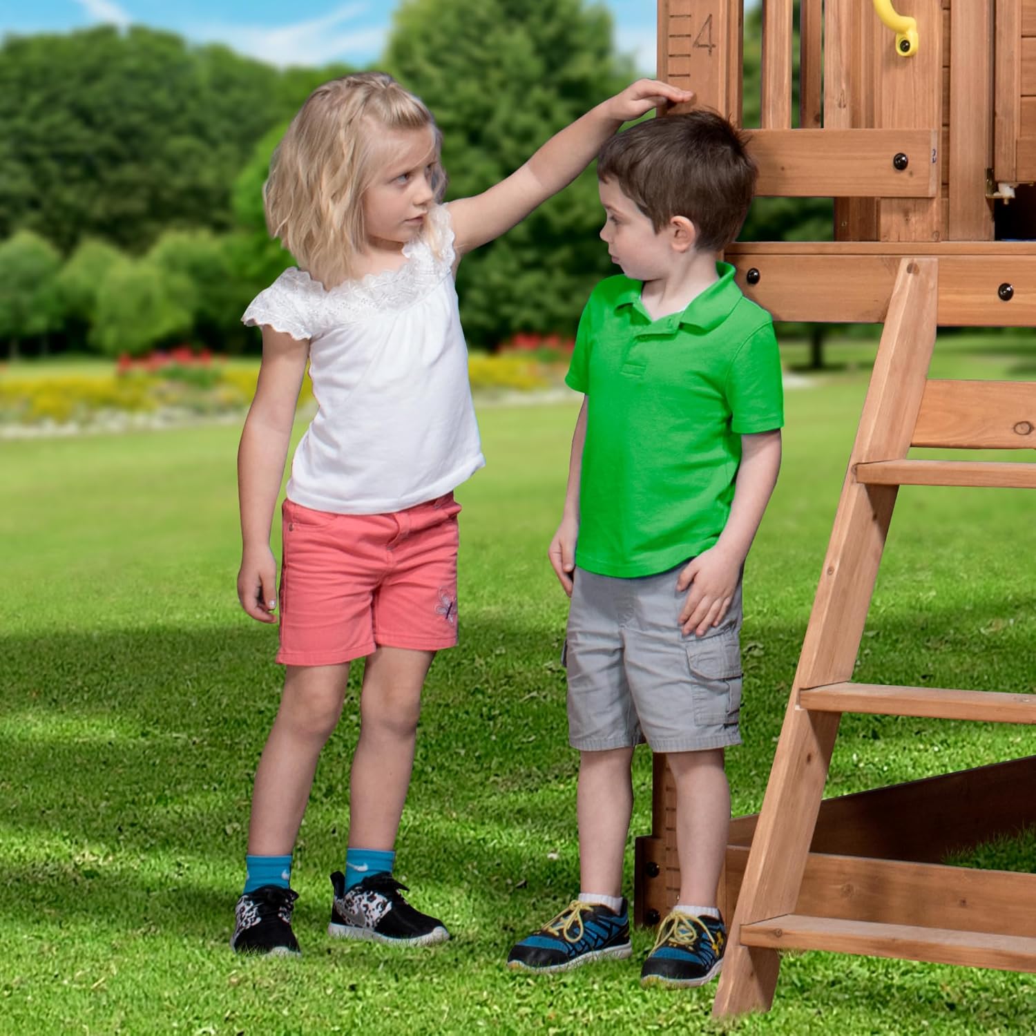 Elevated cedar wooden playhouse with integrated play kitchen, wrap-around deck, and saloon-style doors for outdoor play — view 2