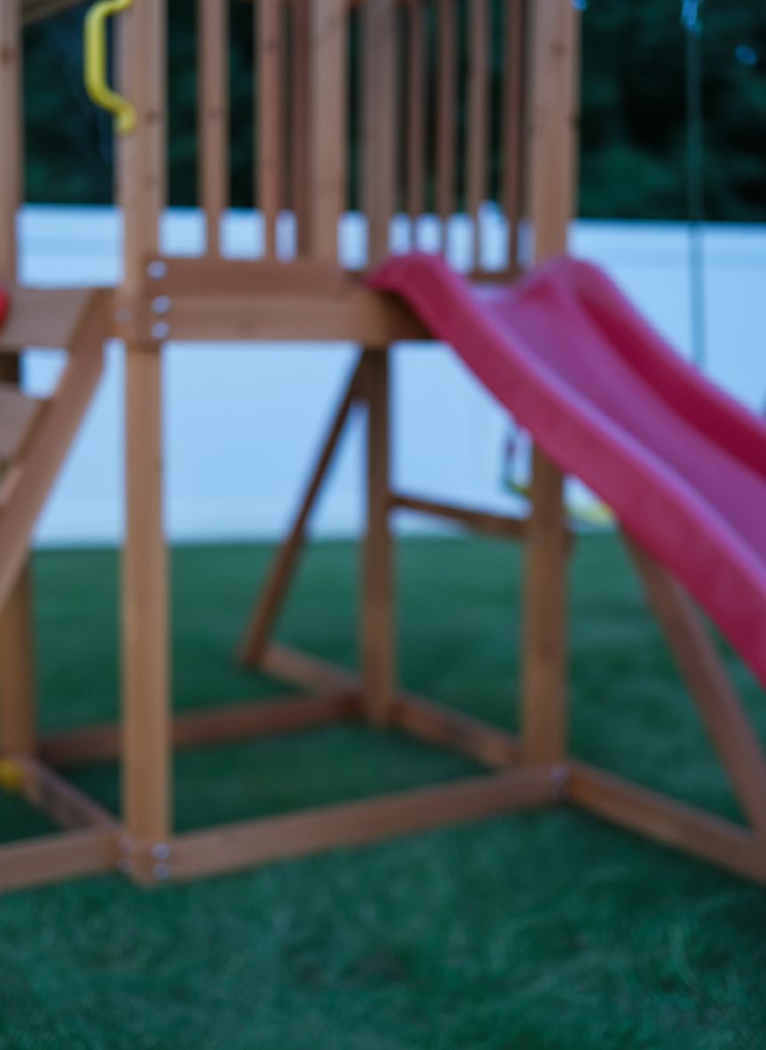 Wooden swing set with canopy featuring two belt swings, wave slide, monkey bars, climbing ladder, and rock wall for backyard play — view 2